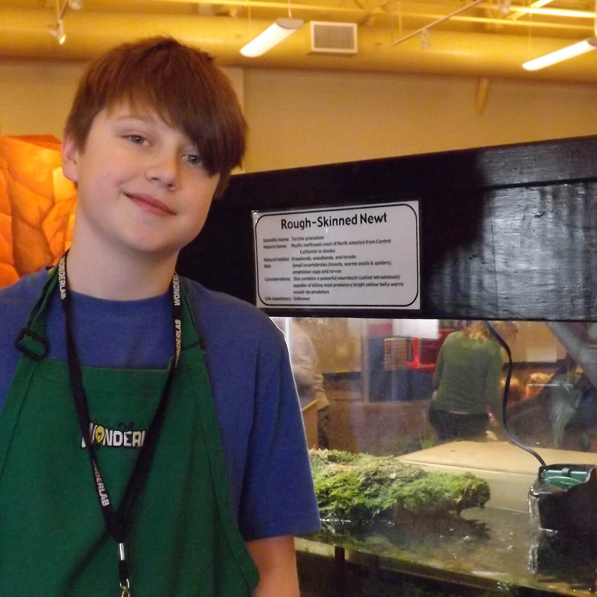Teen volunteer smiles in front of reptile exhibit at Wonderlab Science Museum