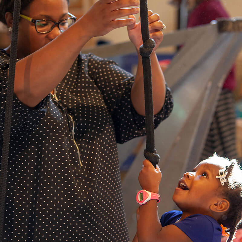 A child smiles as she pulls on a rope, one of Wonderlab's favorite exhibits