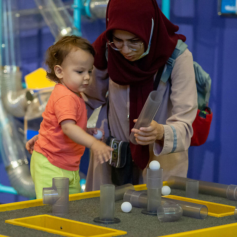 A toddler interacts with the Bernoulli AirTubes exhibit at Wonderlab, while their parent helps
