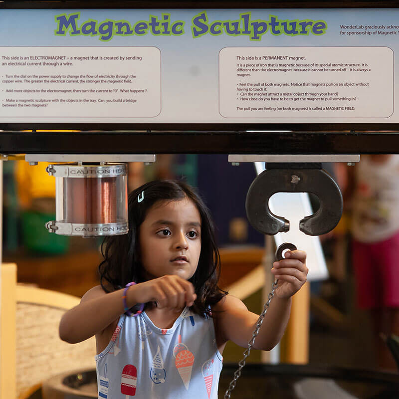 A young girl interacts with Wonderlab's Magnetic Sculpture exhibit