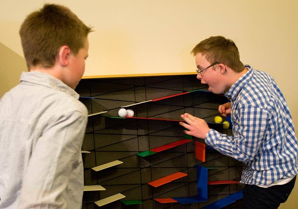Two boys are watching ping pong balls roll down an exhibit at Wonderlab in Indiana