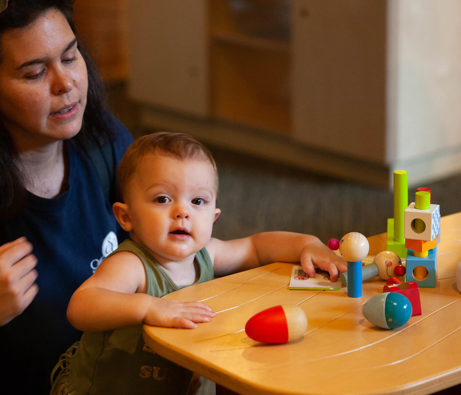 A baby plays with wooden toys at Wonderlab with a caregiver behind them
