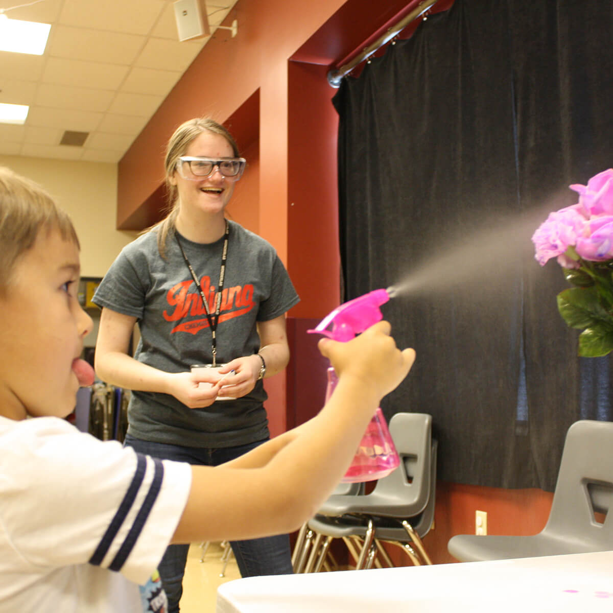 A volunteer laughs as a child sprays a vase of flowers during a field trip to Wonderlab