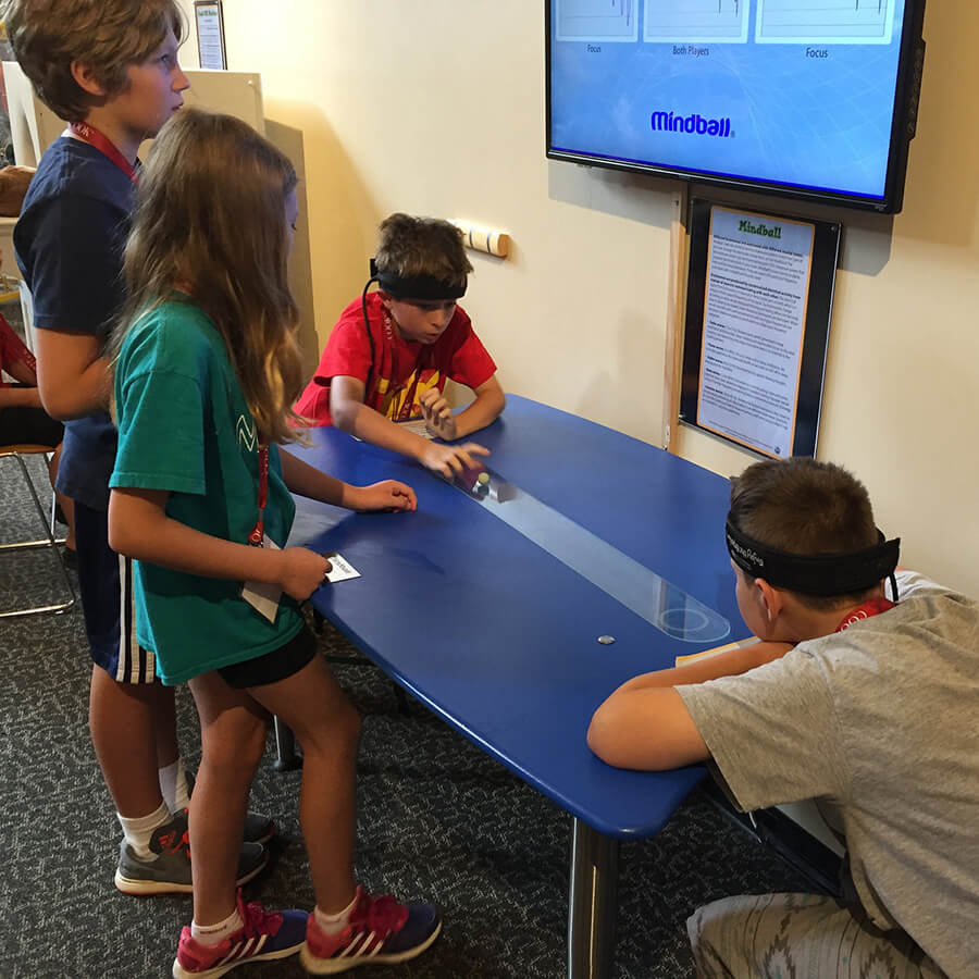 A child interacts with the Wonderlab Mindball exhibit while two other kids and an adult look on