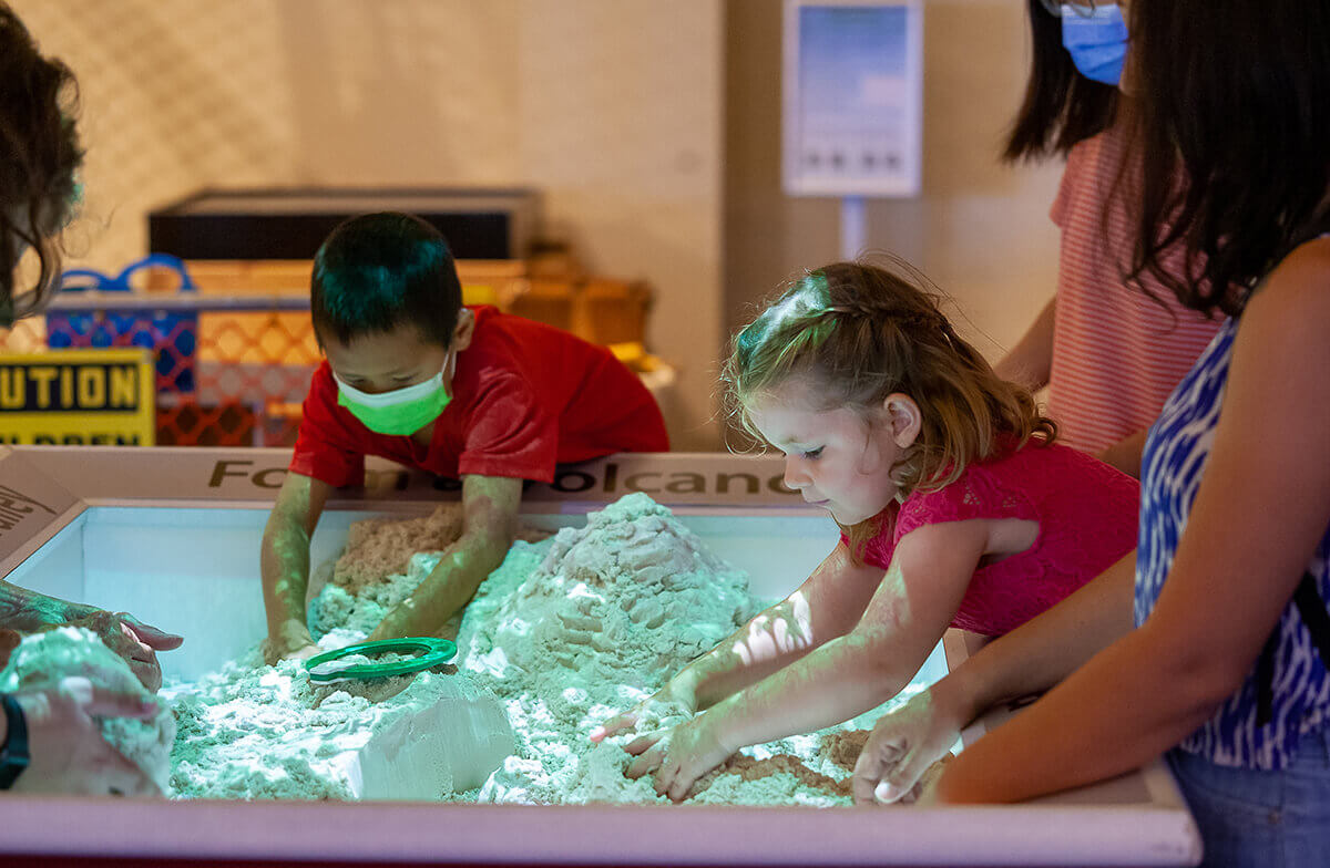 Children and caregivers have their hands in sand, the SandScapes exhibit at Wonderlab