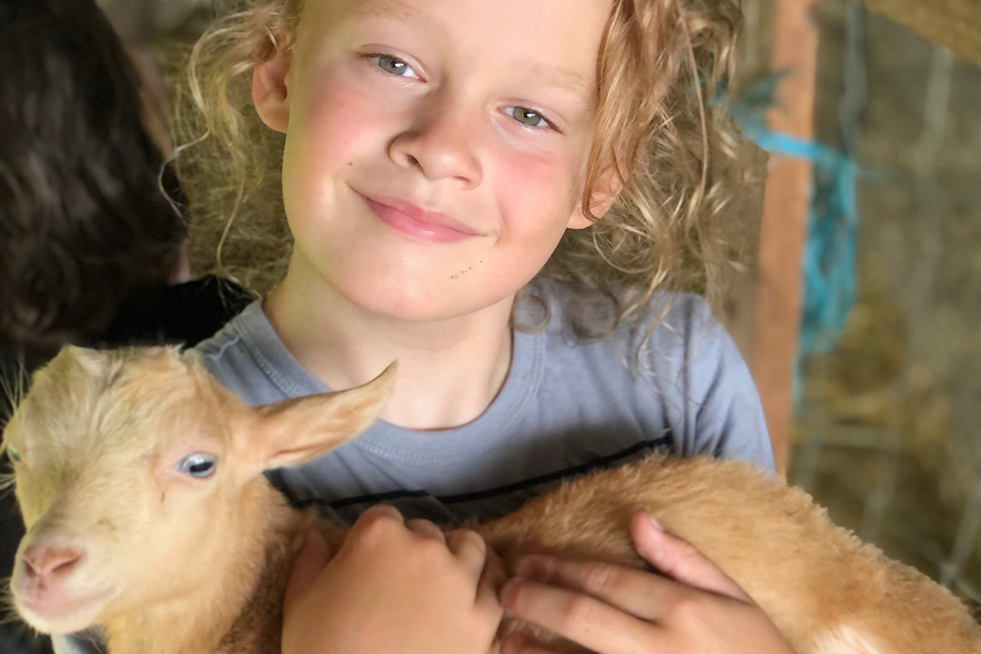 Kid holding a baby goat during summer camp at Goat Conspiracy Bloomington