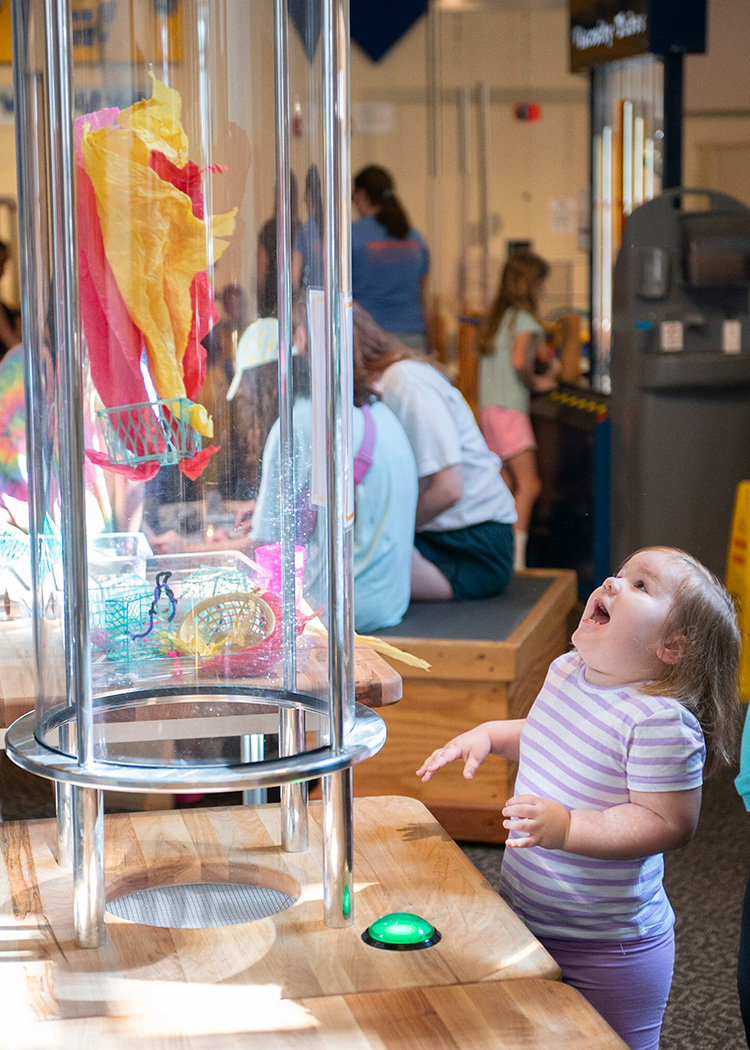 A toddlers exclaims joyfully while watching a craft fly in the translucent tube of the WonderLab HoverCrafts exhibit.