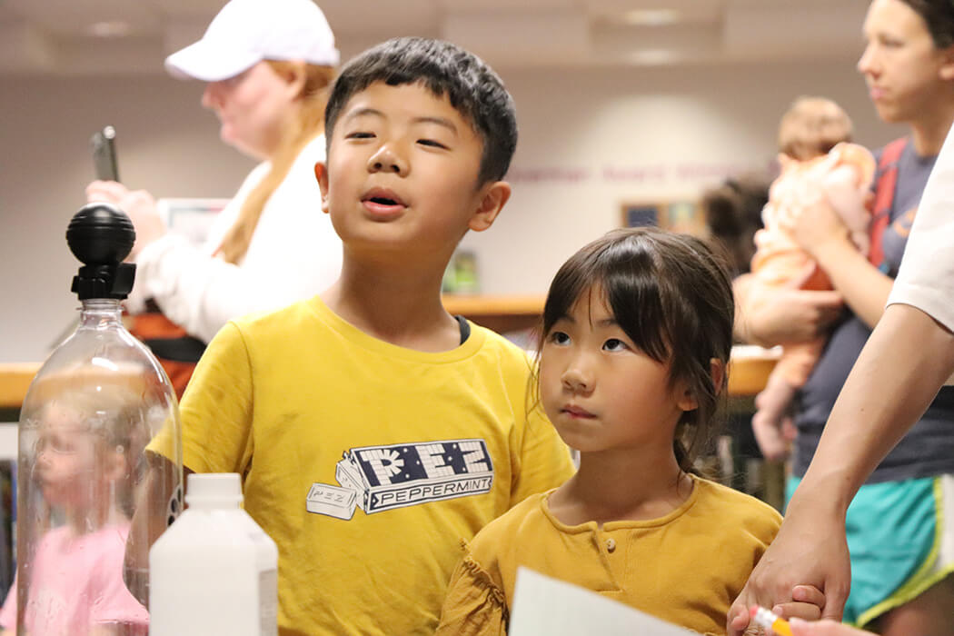 Two children in yellow t-shirts watch intently at WonderLab hands-on science event