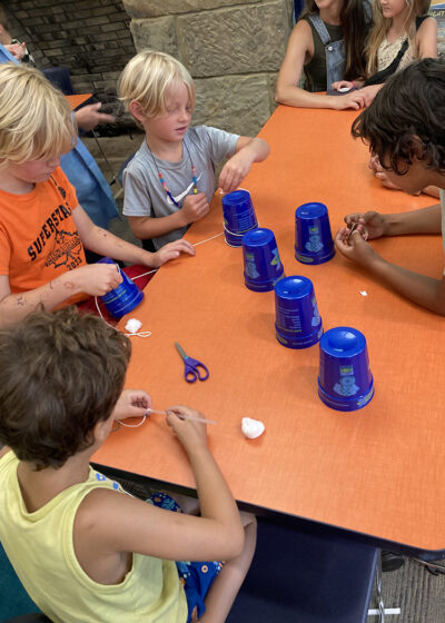A group of children work on an engineering challenge using plastic cups and string during a WonderLab outreach event. 