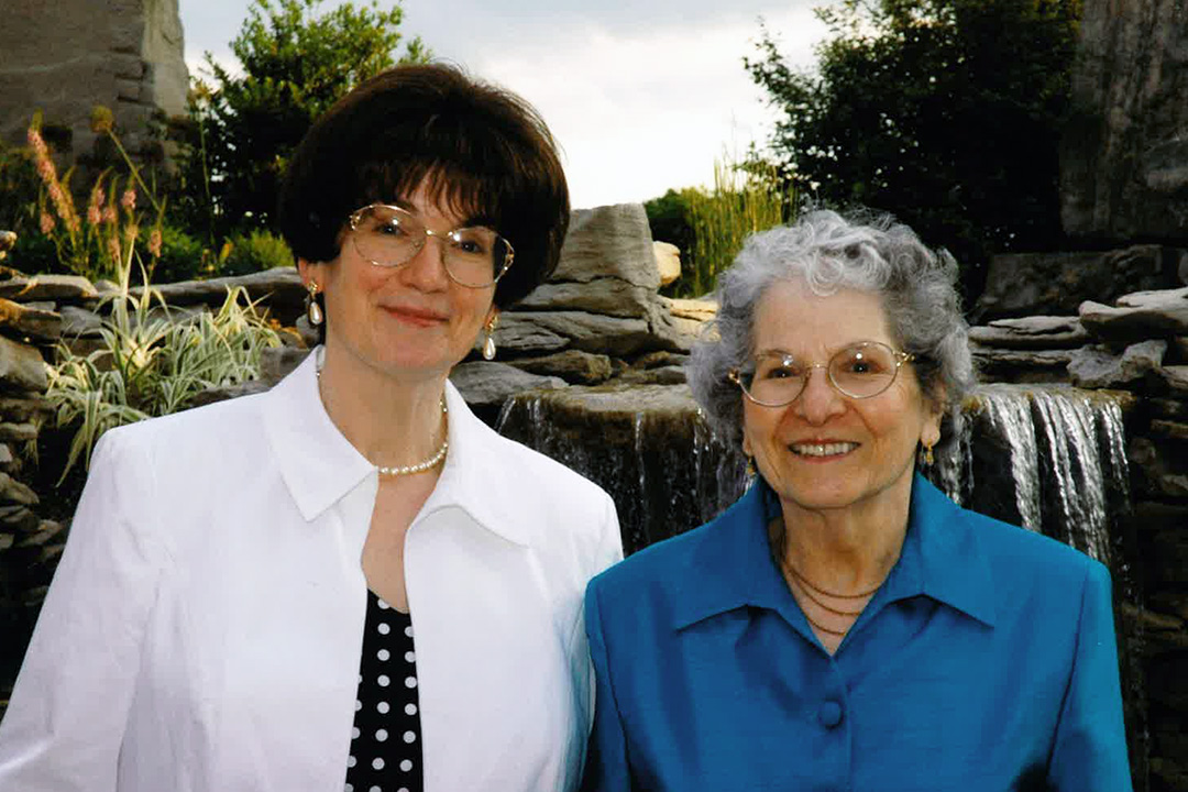 Two white women standing in front of a waterfall. On the left is, middle aged Cathy Olmer, WonderLab Founding Executive Director. On the right is a senior, Norma Olmer, Cathy's mother. Both women are smiling for the camera.